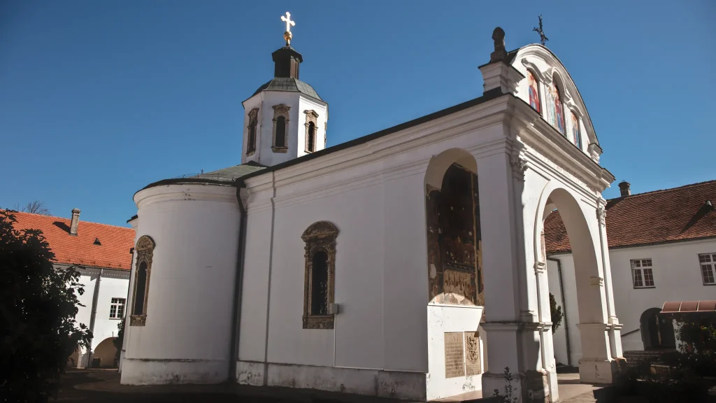 Bela crkva manastira Krušedol sa kubetom i baroknim tremom ispred ulaza, u tremu freske, okolo konaci sa crvenim krovovima
