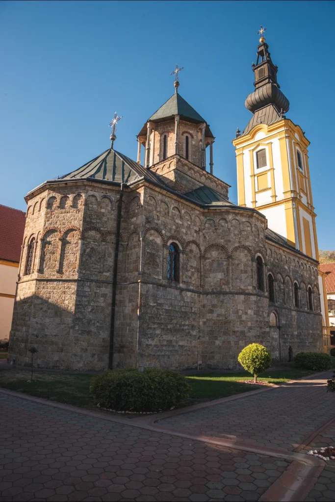 Kamena crkva manastira Privina Glava sa kubetom i visokim žutim zvonikom, ispred nje uređeno dvorište