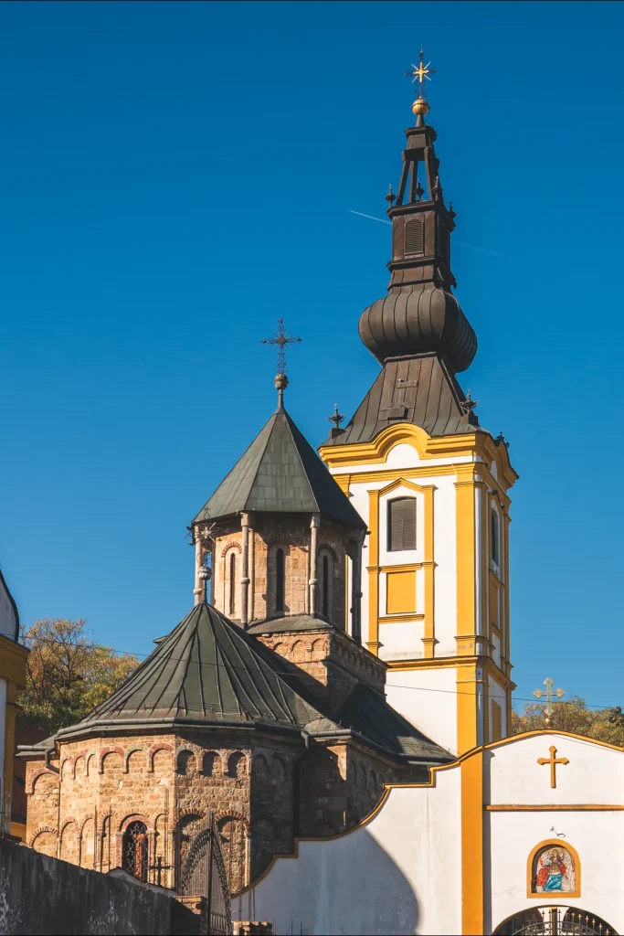 Kube kamene crkve i žuti barokni zvonik manastira Privina Glava iznad bele ulazne kapije