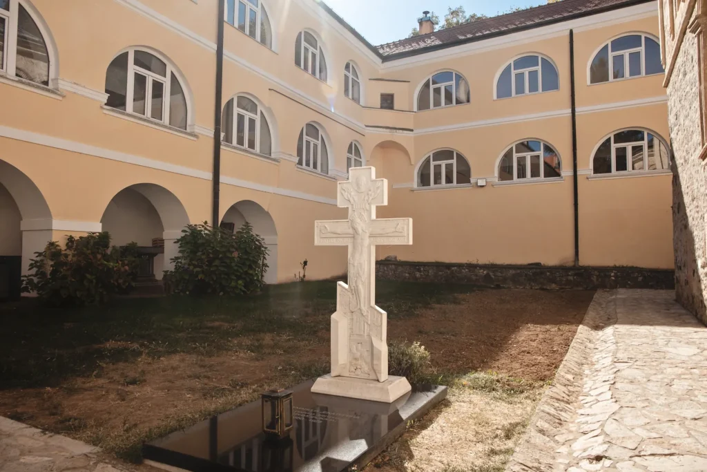 Unutrašnje dvorište manastira Novo Hopovo sa arkadama konaka i belim kamenim krstom na grobu
