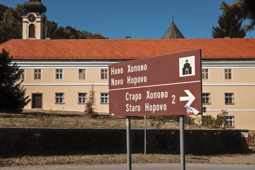 Smeđi turistički putokaz ispred manastira Novo Hopovo, sa strelicom ka Starom Hopovu i brojem 2