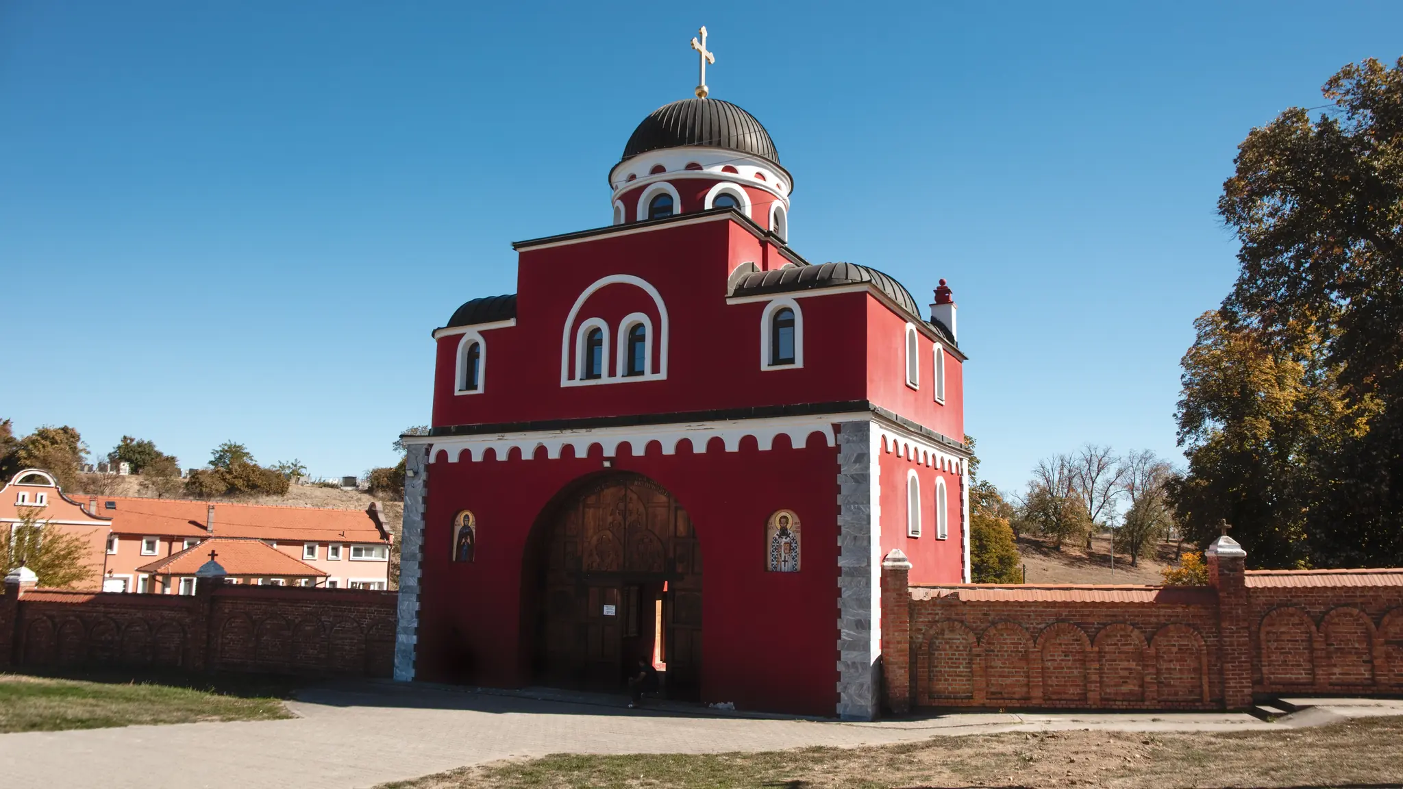 Crvena ulazna kapija manastira Krušedol, zidana u obliku crkve, sa kupolom i krstom